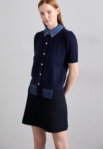 Navy short-sleeve cardigan with cable knit pattern, denim collar, and gold buttons. Black ribbed skirt with denim pocket accents.