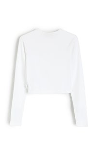 Krótki top z długim rękawem w białej, prążkowanej tkaninie. Posiada okrągły dekolt oraz dopasowane rękawy, z krótkim dołem na wysokości talii.
