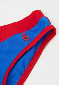 Röda och blå simshorts med en mjuk textur, försedd med en röd logotypaccent. Designen inkluderar kontrasterande färger och en enkel skärning.