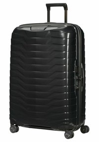 Valise rigide noire avec une surface texturée, motif géométrique, poignée extensible, quatre roues pivotantes et ouverture zippée.