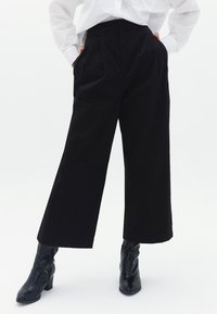 Pantaloni a gamba larga neri in cotone con vita alta, caratterizzati da pieghe frontali e tasche laterali. I dettagli cuciti migliorano la struttura.