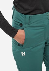 Tauchblaue Outdoor-Hosen mit einer glatten Textur, ausgestattet mit einer seitlichen Tasche mit Reißverschluss, Knopfverschluss und einem sichtbaren Logo am Oberschenkel.