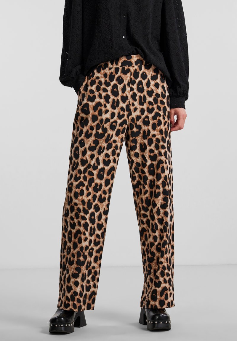 Pantalon à jambes larges imprimé léopard en tissu beige et noir, avec une texture lisse. Associé à un chemisier noir ample à manches longues.