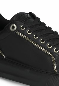 Czarne skórzane sneakersy z czarnymi sznurówkami, srebrnymi oczkami, ozdobnymi srebrnymi ćwiekami wzdłuż boku oraz markowym metalowym detalem blisko góry.