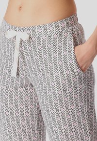 Pantalones blancos con estampado de zigzag negro y formas de diamante rosa. Cuentan con una cintura con cordón y bolsillos laterales. Hechos de tela suave.