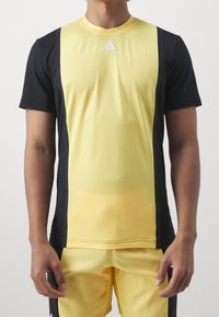 Camiseta atlética amarilla y negra de manga corta, con textura acanalada y escote redondo. Presenta un logo de Adidas en el pecho.