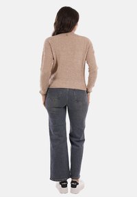 Maglione beige a coste con maniche lunghe, scollatura rotonda, abbinato a jeans dritti blu scuro e sneakers bianche con dettagli neri.