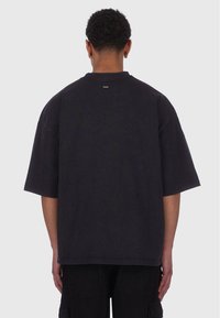 Sort oversized t-shirt med korte ærmer, lavet af bomuldsmateriale, simpel crew neck-design og et diskret logo ved bunden af nakken.