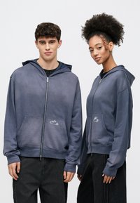 Tengerészkék cipzáros kapucnis pulóver puha anyagból, elülső zsebbel, logóval és csillagmintával. Húzózsinóros kapucnival és bordázott mandzsettákkal rendelkezik.