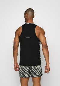 Černý bezrukávový top s bílým vodorovným pruhem na zádech, doplněný šedými a zelenými kostkovanými šortkami. Hladká tkanina s atletickým střihem.