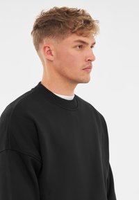 Svart crewneck sweatshirt med avslappnad passform, ribbat nacke och sänkta axlar, som har en slät yta och en minimalistisk design.