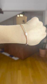 Pulsera de oro rosa con una delicada cadena de plata y un pequeño cierre decorativo, llevada en una muñeca sobre un suelo de madera clara.