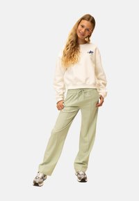 Lichtgroene joggingbroek met een elastische tailleband, gecombineerd met een wit sweatshirt met een kleine blauwe afbeelding op de borst.