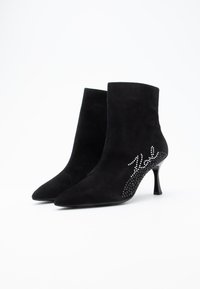 Botas de tornozelo em camurça preta com bicos pontiagudos, saltos agulha e detalhes decorativos em strass nas laterais. Textura suave em toda a parte.