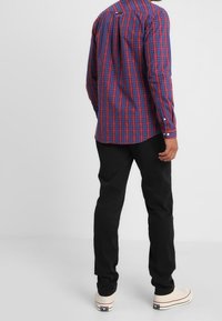 Långärmad rutig skjorta i blått, rött och vitt; knappad krage; ihopparad med svarta byxor och vita sneakers; synlig detalj av skjortetikett.