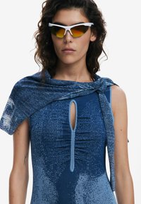 Sleeveless blue dress with ruched texture, keyhole neckline, and a patterned blue wrap. Model wearing white sports sunglasses with tinted lenses.