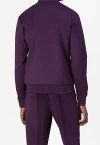 Sudadera morada con textura suave, puños acanalados y cuello alto, combinada con pantalones ajustados a juego. Diseño minimalista, sin estampados.