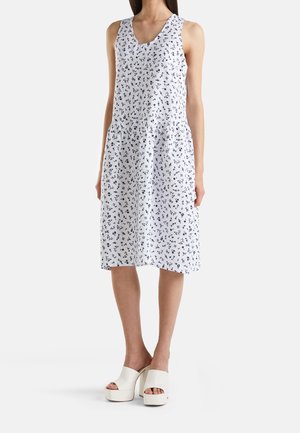 Robe midi blanche sans manches avec imprimé floral noir petit, portée avec des chaussures à plateforme blanches à talons hauts et orteils ouverts.