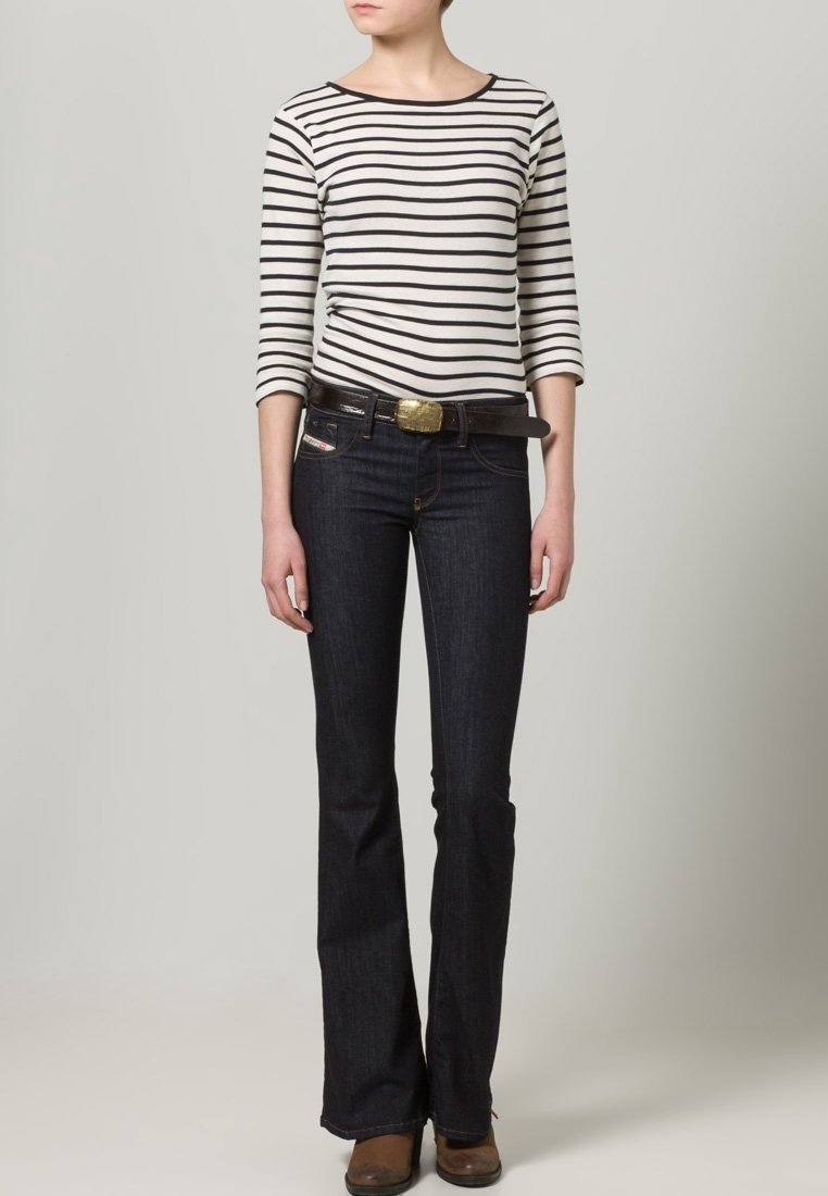 W paski bluzka z długim rękawem w kolorze kremowym i czarnym, zestawiona z ciemnoniebieskimi dżinsami z rozszerzanymi nogawkami. Brązowy pasek z złotą klamrą i brązowe buty.