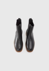 Bottes noires en cuir à hauteur de cheville avec une texture lisse, un bout arrondi et des panneaux latéraux élastiques. Présente une semelle en caoutchouc marron. Hauteur standard.