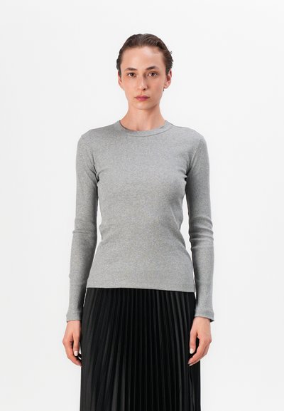 Haut à manches longues en maille ribbed gris avec un col rond, associé à une jupe plissée noire, mettant en valeur la douceur de la texture et la coupe ajustée du haut.