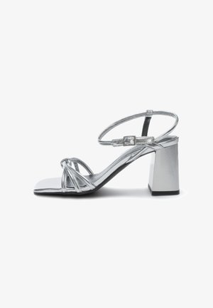 Sandalias de tacón alto plateadas con punta cuadrada, tiras metálicas, correa de tobillo plana y tacón grueso. Textura suave y superficie reflectante.
