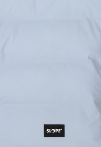 Vaaleansininen trekkaustakki vaakasaumalla ja mustalla logotarralla, jossa lukee 'SLOPE'. Suuri, sileä rakenne, keskitetty muotoilu edessä.