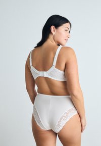 Soutien-gorge en dentelle blanche avec des bretelles réglables et une fermeture à crochets, associé à une culotte blanche taille haute avec des accents en dentelle sur les côtés.