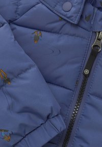 Blå puffjacka med quiltad textur, med skidteman i orange och grönt. Inkluderar svart dragkedja och knappstängning.