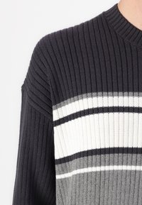 Ribbed knit sweater features dark gray, white, and light gray horizontal stripes. Round neckline and dropped shoulder design enhance texture.