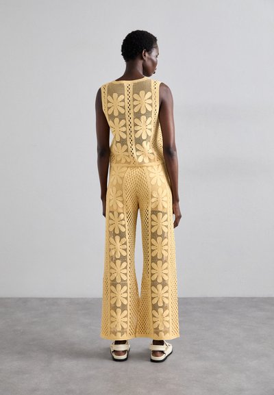 Ensemble en tricot jaune en deux pièces avec un motif floral, présentant des motifs en maille ouverte, un pantalon à jambes larges et un haut à encolure dégagée.