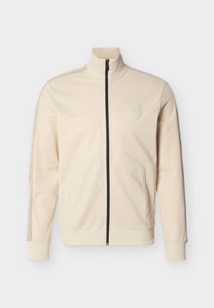 Κρεμ μπουφάν με φερμουάρ, ψηλό γιακά, ριμπ μανσέτες και πλαϊνές τσέπες. Διαθέτει διακριτικό λογότυπο και αντίθετο μαύρο φερμουάρ.