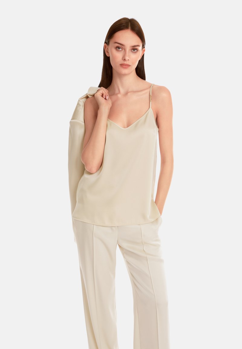 Beige Satincamisole mit dünnen verstellbaren Trägern und einem leichten V-Ausschnitt, kombiniert mit cremefarbenen, weiten Hosen. Glatte Textur insgesamt.