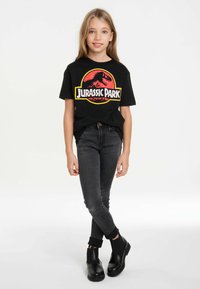 Black cotton t-shirt featuring a colorful Jurassic Park graphic, paired with dark denim jeans and black ankle boots.