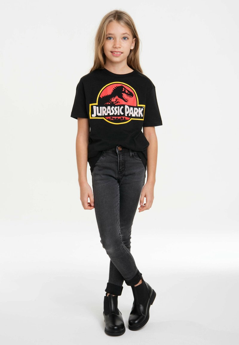 Black cotton t-shirt featuring a colorful Jurassic Park graphic, paired with dark denim jeans and black ankle boots.