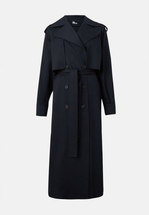 Longue trench-coat noir à double boutonnage avec larges revers, ceinture, détails à boutons et épaulettes sur un fond uni.
