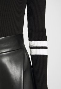 Pull noir à côtes avec des accents rayés blancs au niveau des poignets, associé à une jupe noire en simili cuir taille haute avec une finition glossy.