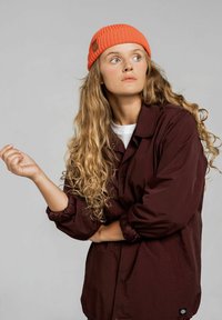 Burgundowa kurtka zapinana na guziki o luźnym kroju, z okrągłym kołnierzem i elastycznymi mankietami. Połączona z jasnopomarańczową wełnianą czapką.