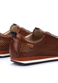 Scarpe slip-on in pelle marrone con design perforato, suola arancione e bianca a contrasto, e dettaglio del logo sul lato. Finitura testurizzata.