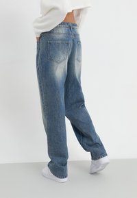 Light blue denim jeans with a relaxed fit, featuring fading and two back pockets. Styled with a white top and white sneakers.