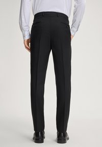 Schwarze Anzughose mit geradem Schnitt, ausgestattet mit zwei hinteren Taschen mit Knöpfen. In Kombination mit schwarzen Schuhen wirkt der Stoff glatt und maßgeschneidert.