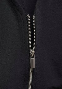 Black zip-up jacket featuring a metal zipper, grey teeth, and a smooth fabric texture. The zipper pull is rectangular and metallic.