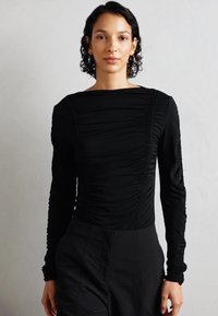 Camiseta negra de manga larga con detalles fruncidos, escote cuadrado y diseño ajustado, confeccionada en un tejido elástico con textura suave.