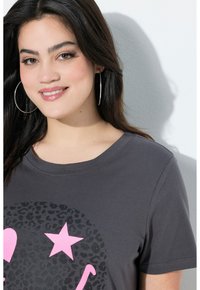 T-shirt gris charbon avec un imprimé léopard noir rond, une étoile rose et des graphiques de cœur. Manches courtes, encolure ronde, matière en coton.