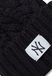 Mustat neulepipo, jossa on teksturoitu kuvio. Varustettu valkoisella tarralla mustalla graafisella suunnittelulla. Pehmeä, lämmin materiaali talvivaatteita varten.