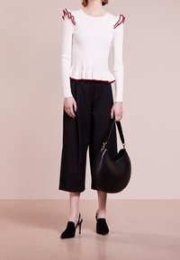 Weißes, geripptes Langarmoberteil mit roten Rüschenakzenten, schwarze, cropped Hosen, schwarze, hohe Mules und eine große schwarze Hobo-Tasche.