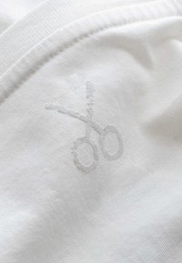 Witte stof met een subtiele geborduurde schaarmotief in een iets lichtere tint, die de textuur en het zachte weefpatroon accentueert.