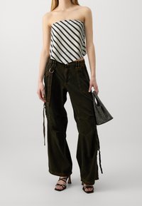 Haut sans bretelles rayé en blanc et marine ; pantalon cargo ample de couleur olive foncée avec poches latérales ; sac à main noir texturé ; sandales noires à lanières.