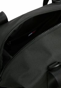 Borsa in tessuto nero con chiusura a zip, caratterizzata da una superficie testurizzata, cuciture robuste e ferramenta visibile lungo la cerniera.