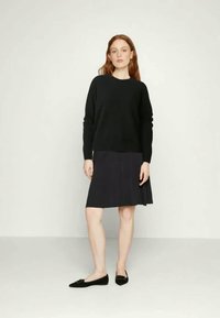 Melna džemperis ar apaļu dekoltē, kombinēts ar tumši pelēku zvanu svārku. Modelis valkā melnas plakanas kurpes, ar garām, viļņotām sarkani brūnām matiem.